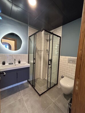 A modern bathroom with a glass-enclosed shower, a sink with a mirror, and a toilet. - Avlu Villas & Apartments (Kemer)
