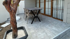 Un patio con mesa y sillas, un árbol en maceta y una ventana con cortinas.