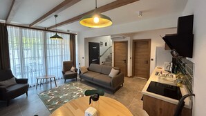 Una sala de estar moderna con un sofá, sillones, una mesa de centro y un comedor. Hay una escalera que lleva a otro nivel, y una zona de cocina con un fregadero y encimera.
