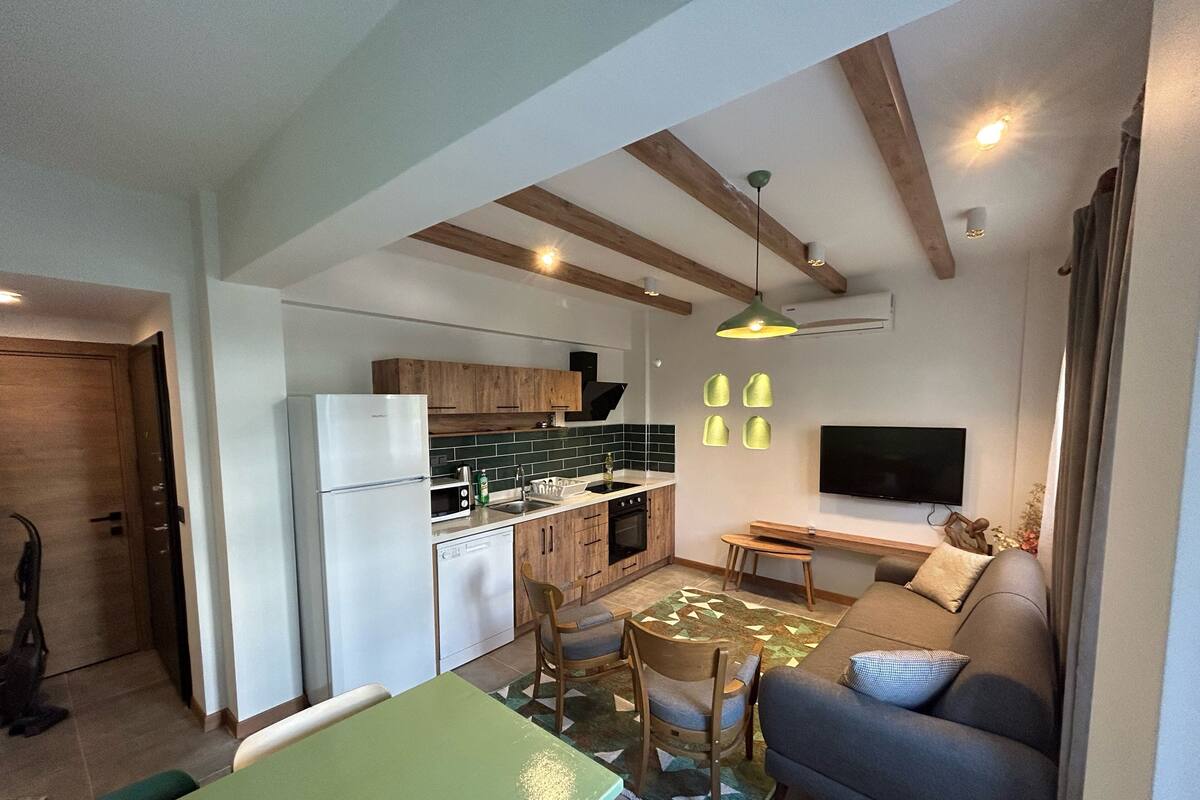 Eine moderne Küche mit Holzschränken, einem eingebauten Ofen und einem Essbereich mit grünem Tisch und Stühlen.
