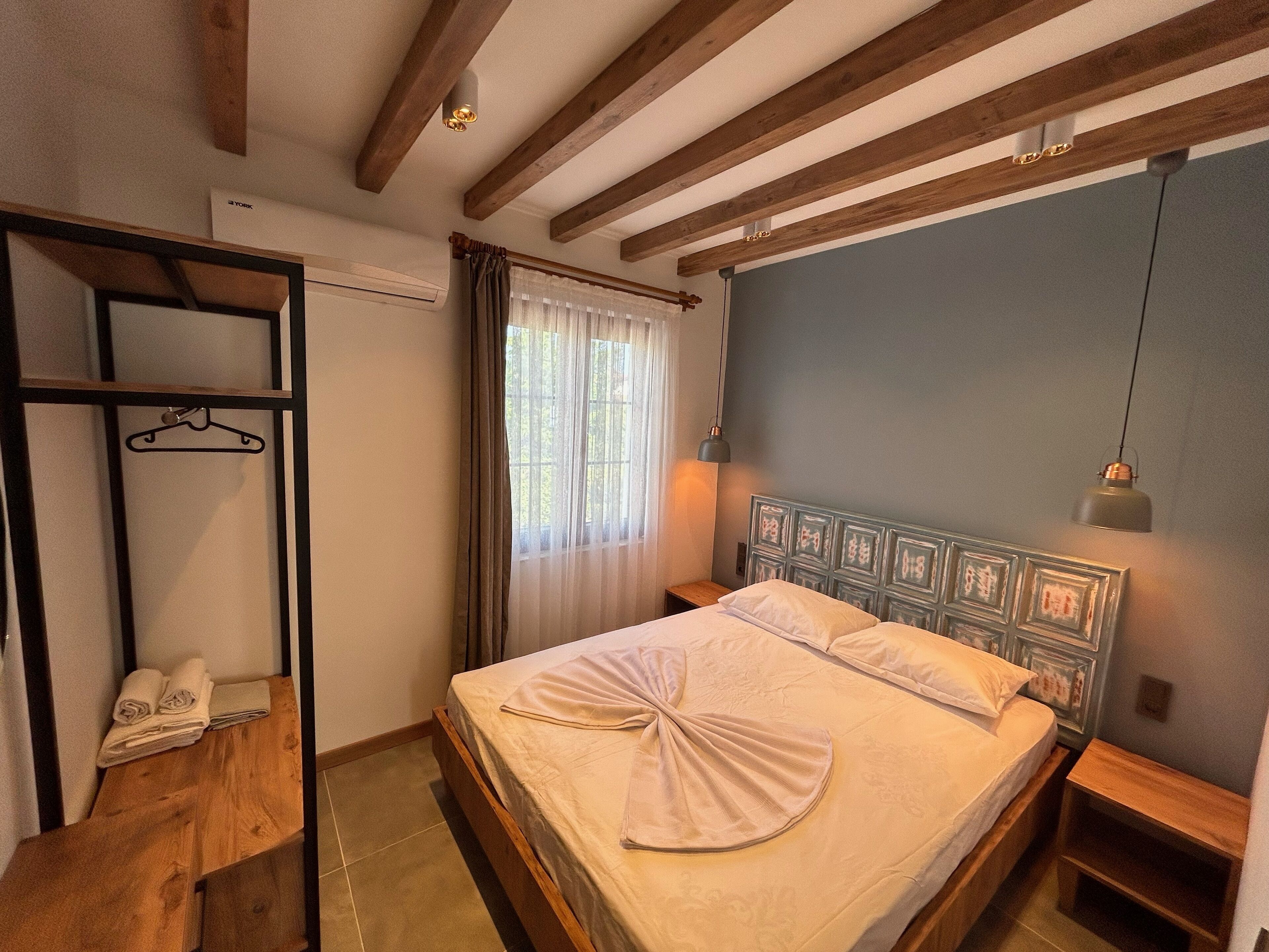 Un dormitorio con cama de madera, un armario con perchero y una ventana con cortinas.