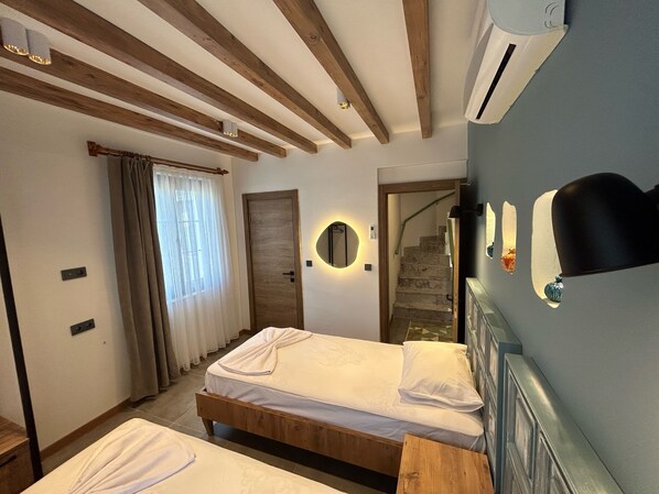 A bedroom with two beds, wooden beams on the ceiling, a staircase, and a wall-mounted mirror. - Avlu Villas & Apartments (Kemer)