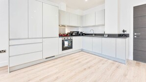 A modern kitchen with white cabinets, a black countertop, and a wooden floor. - Stylish 2BR Solihull Flat, Quick Train to NEC (Birmingham)