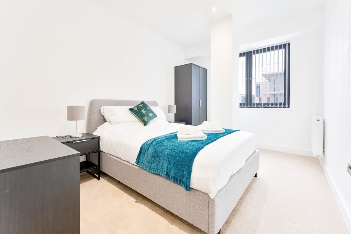 Ein modernes Schlafzimmer mit Bett, Nachttisch, Kleiderschrank und einem Fenster mit Gitterstäben.