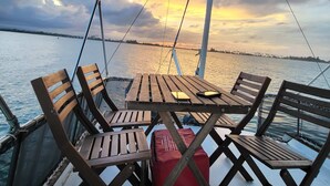 A boat deck with wooden chairs and a table, a red cushion, and a white cup on the floor. - Cozy Room | Walk to La Placita & Condado Beach (San Juan)