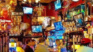 A bar with multiple televisions, a variety of bottles, and a sign reading "Ocean Pky". - Cozy Room | Walk to La Placita & Condado Beach (San Juan)