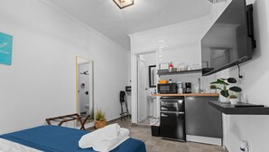 A compact hotel room with a bed, a kitchenette, a mirror, and a small bathroom. - Cozy Room | Walk to La Placita & Condado Beach (San Juan)