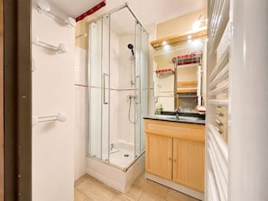 A bathroom with a glass-enclosed shower, a sink, and wooden cabinets.
