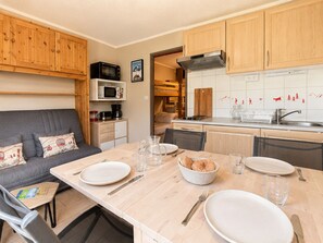 A compact kitchen with wooden cabinets, a microwave, and a dining area with a table set for two.