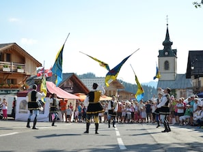 A street parade with participants in traditional costumes, a crowd of spectators, and a church in the background.