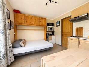 Una stanza funzionale con un letto, angolo cottura, mobili in legno e ventilatore a soffitto.