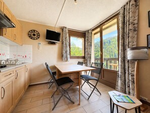 Una stanza con un tavolo di legno, sedie, un televisore e una finestra vista alberi.