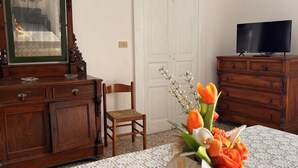 Ett rum med en byrå i trä, en stol, en tv-apparat som står på ett träskåp och en vas med blommor på ett bord.