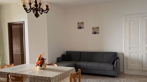 En matplats med ett bord för fyra personer, en grå soffa och två konstverk som hänger på väggen.