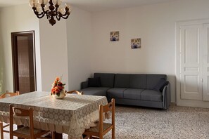 A dining area with a table set for four, a grey sofa, and two wall-mounted artworks.
