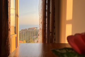 A view from a window with curtains, overlooking a cityscape with buildings and a clear sky.