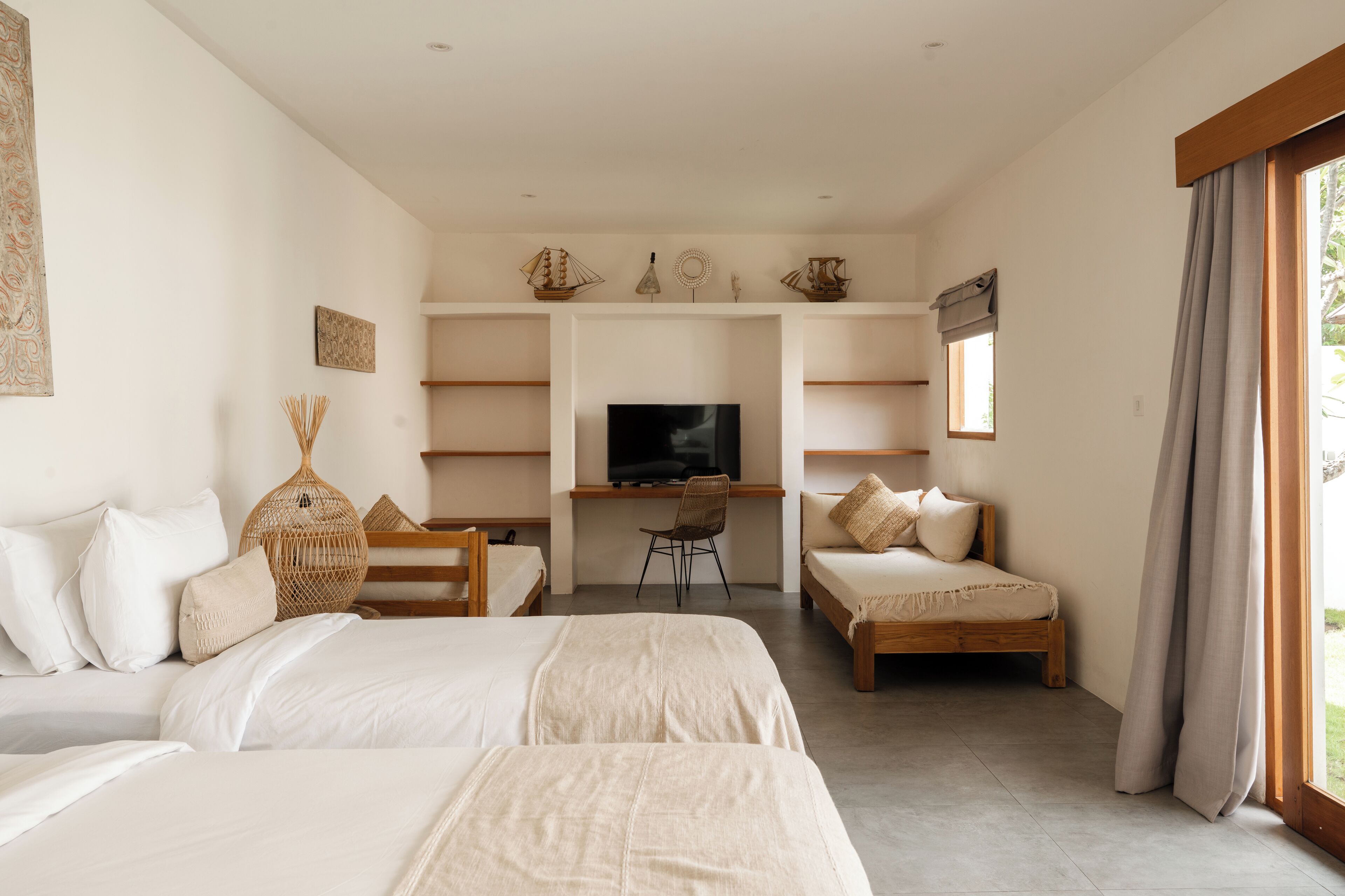 A bedroom with two beds, a desk, a TV, and a window with curtains.