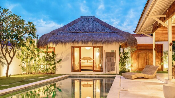 Un bungalow au toit de chaume doté d’une piscine et d’un espace détente.