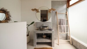 Une salle de bain avec un miroir rond, un lavabo rond, un porte-serviettes et une échelle en bois.