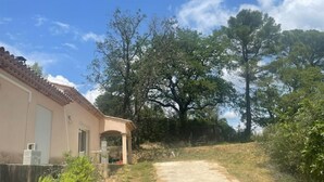 A house with a beige exterior and a tiled roof, a covered porch, and a dirt path leading to a wooded area. - Villa au Calme (Draguignan)