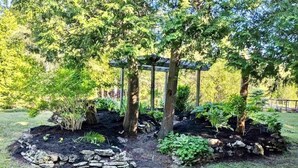 Ein Garten mit einem Kiesweg, der zu einer Pergola inmitten von Bäumen und Pflanzen führt.