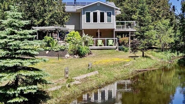 Ein zweistöckiges Haus mit Veranda, einer kleinen Terrasse und einem Teich im Vordergrund.
