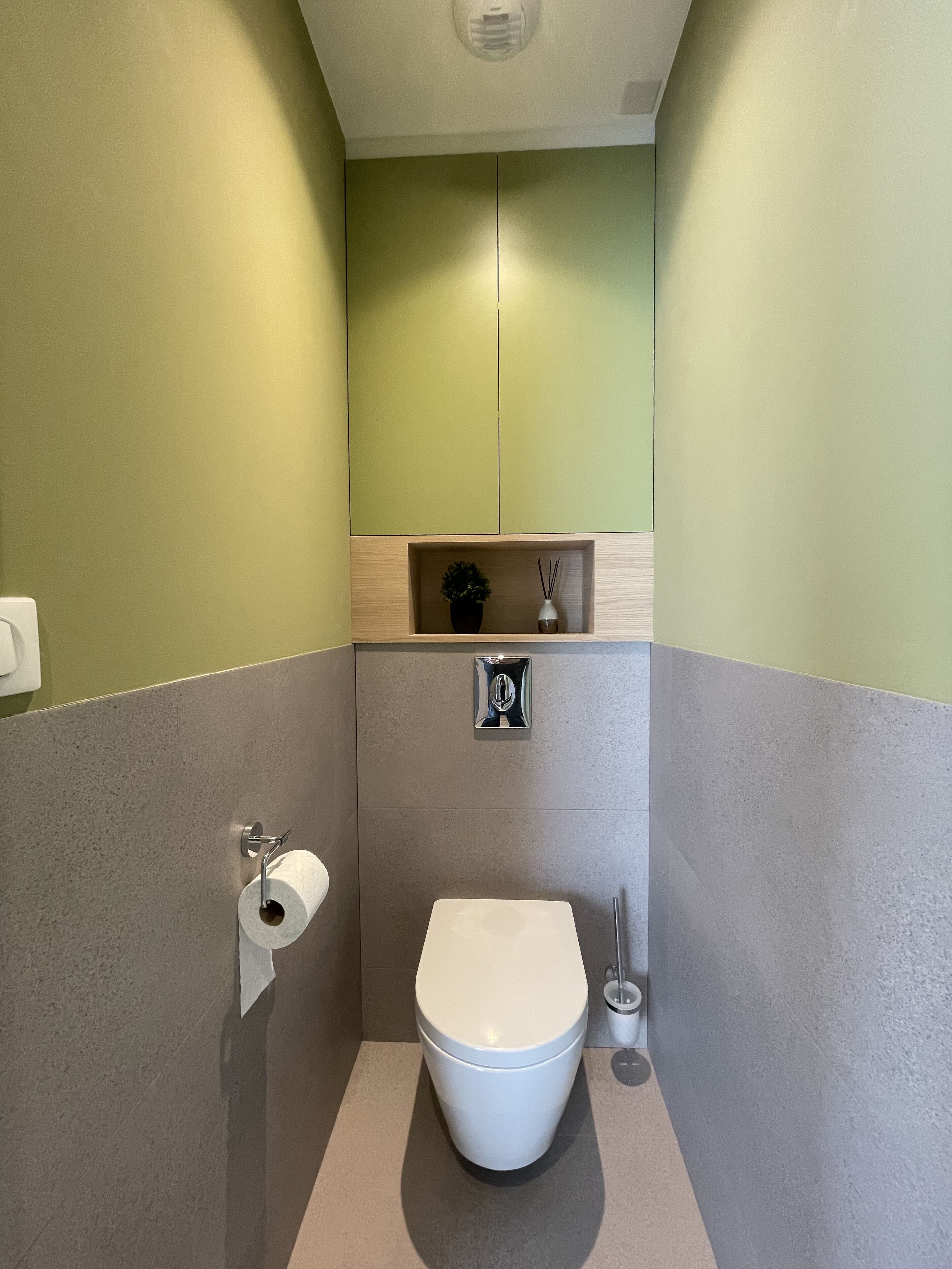 Un baño compacto con inodoro, un pequeño estante con planta en maceta y un dispensador de papel higiénico.