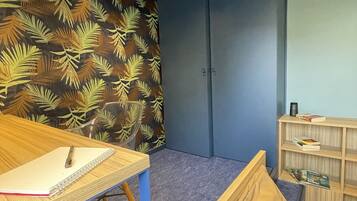 A room with a bed, a desk with a notebook, a shelf with books, and a wall with a leaf pattern.
