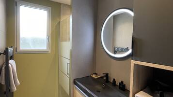 Une salle de bain moderne avec un grand miroir, un lavabo et un espace douche.