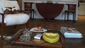 Ein Wohnzimmer mit einem großen abstrakten Gemälde, einem fellbezogenen Sessel, einem Couchtisch mit Zeitschriften und einem roten Akzentstuhl.