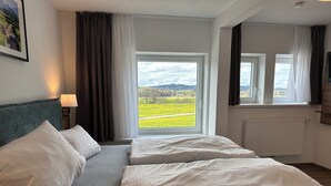 A double bed with white linens, a nightstand with a lamp, and a window with a view of a green field.