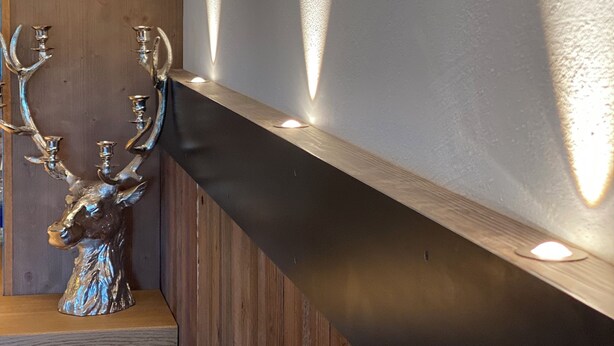 A modern interior with a wooden bench and a metallic deer sculpture.