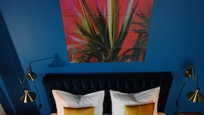 A double bed with white linens and two pillows, a blue headboard, and a vibrant abstract painting on the wall. - Bohème Historic | City | 100m2 | Netflix (Landshut)