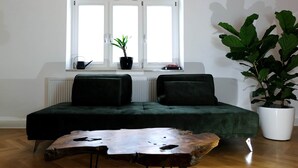 A room with a green sofa, a wooden coffee table, a large window with a plant on the sill, and a radiator below. - Bohème Historic | City | 100m2 | Netflix (Landshut)