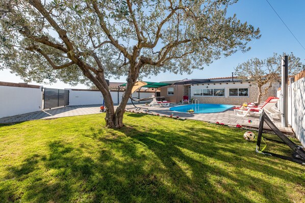 Un jardin avec une piscine, un arbre et une maison.