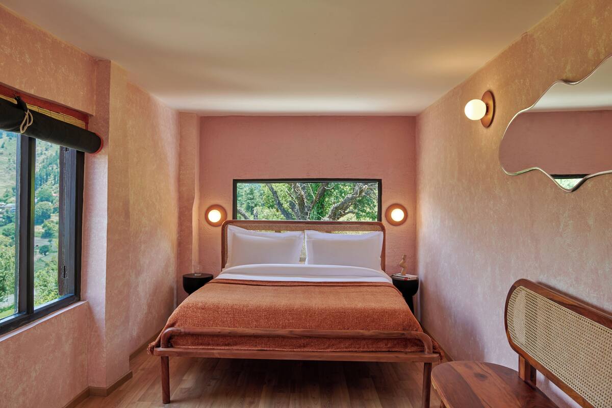 Ein Schlafzimmer mit einem Bett, einem Fenster, einem Nachttisch und einem wandmontierten Spiegel.