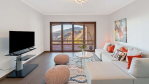 A modern living room with a flat-screen TV, a sofa with colorful cushions, a coffee table, and a view of mountains through large sliding doors. - Elegant Luxury Villa with Stunning Mediterranean Views (La Herradura)