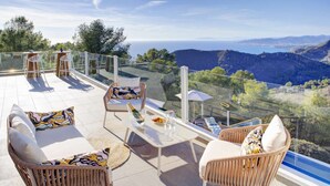 A terrace with wicker furniture, a glass table, and a view of the sea and mountains. - Elegant Luxury Villa with Stunning Mediterranean Views (La Herradura)