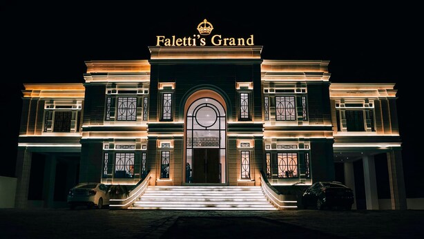Ein prächtiges Gebäude mit einem markanten Eingang, beleuchtet durch warmes Licht, mit der Aufschrift "Paletti's Grand" oben.
