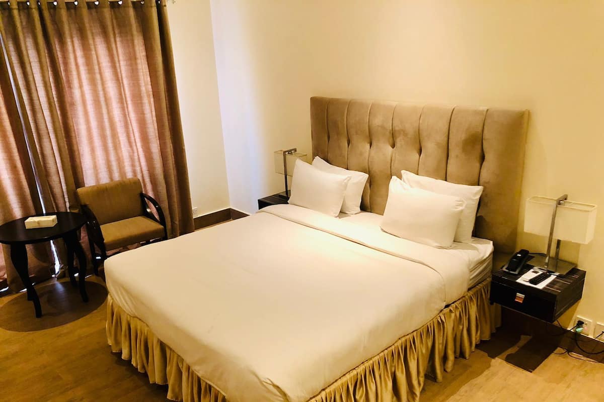 Une chambre d’hôtel avec un grand lit, une chaise, une table de chevet et une lampe.