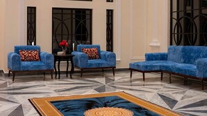 Eine geräumige Lobby mit hoher Decke, einer großen blauen Sofagarnitur, einem gemusterten Teppich und einem Kamin.