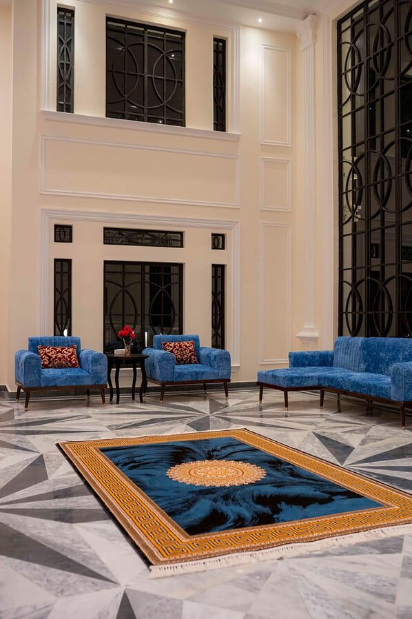 A spacious lobby with a high ceiling, a large blue sofa set, a patterned rug, and a fireplace.