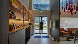 A modern lobby with a wooden reception desk, framed pictures, potted plants, a mural, and a view of the outside. - ST Signature Bugis Middle (Singapore)