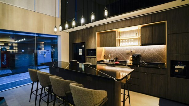 A modern kitchen with a bar area, equipped with a coffee machine, and a view of the street outside. - ST Signature Bugis Middle (Singapore)