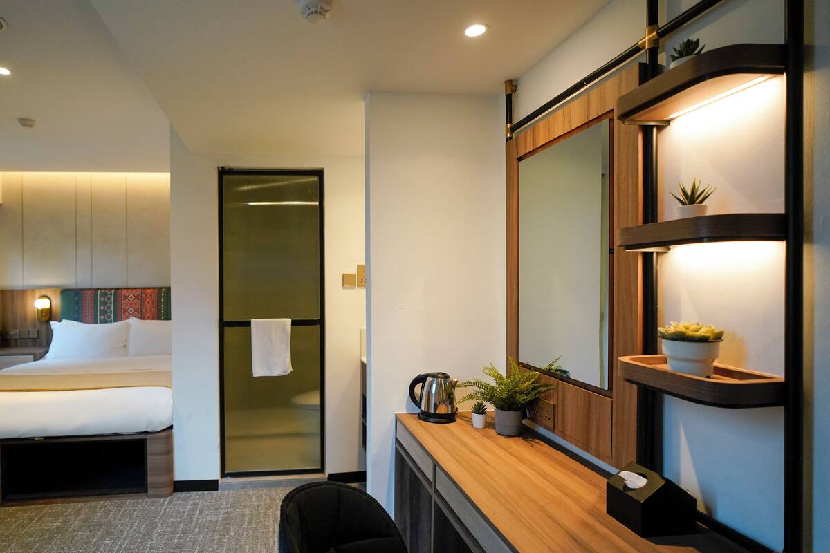 A modern hotel room with a bed, a desk with a mirror, and a small plant.