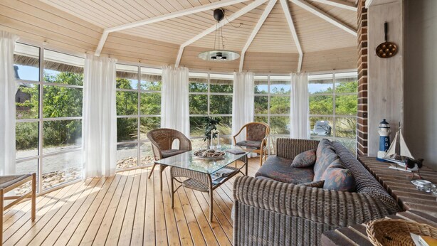 A sunroom with a wooden ceiling, large windows, wicker furniture, and a small model ship. - 4 bedroom gorgeous home in Rømø (Rømø)