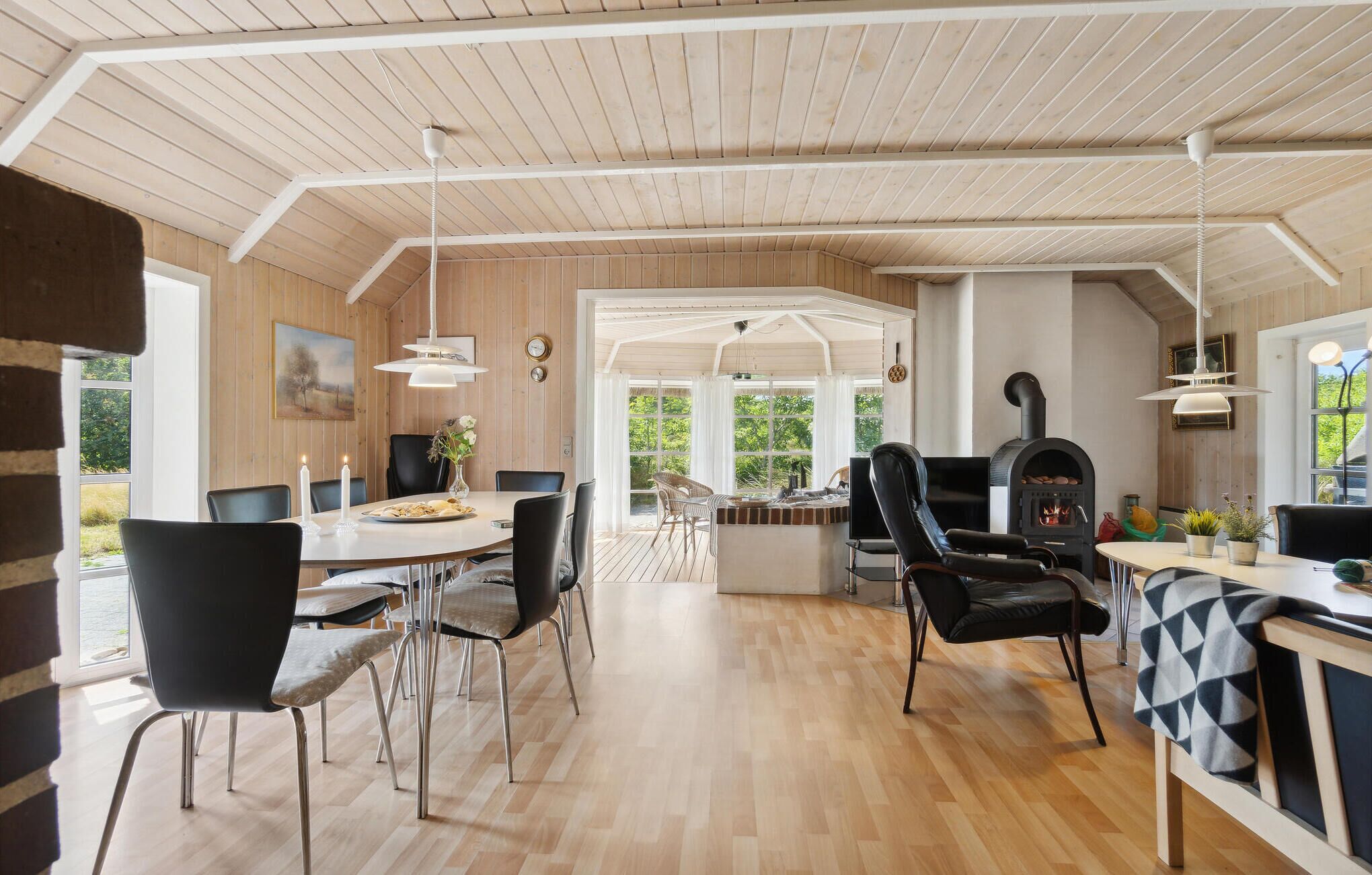 A spacious room with a wooden ceiling, a fireplace, and a dining area with chairs and a table.