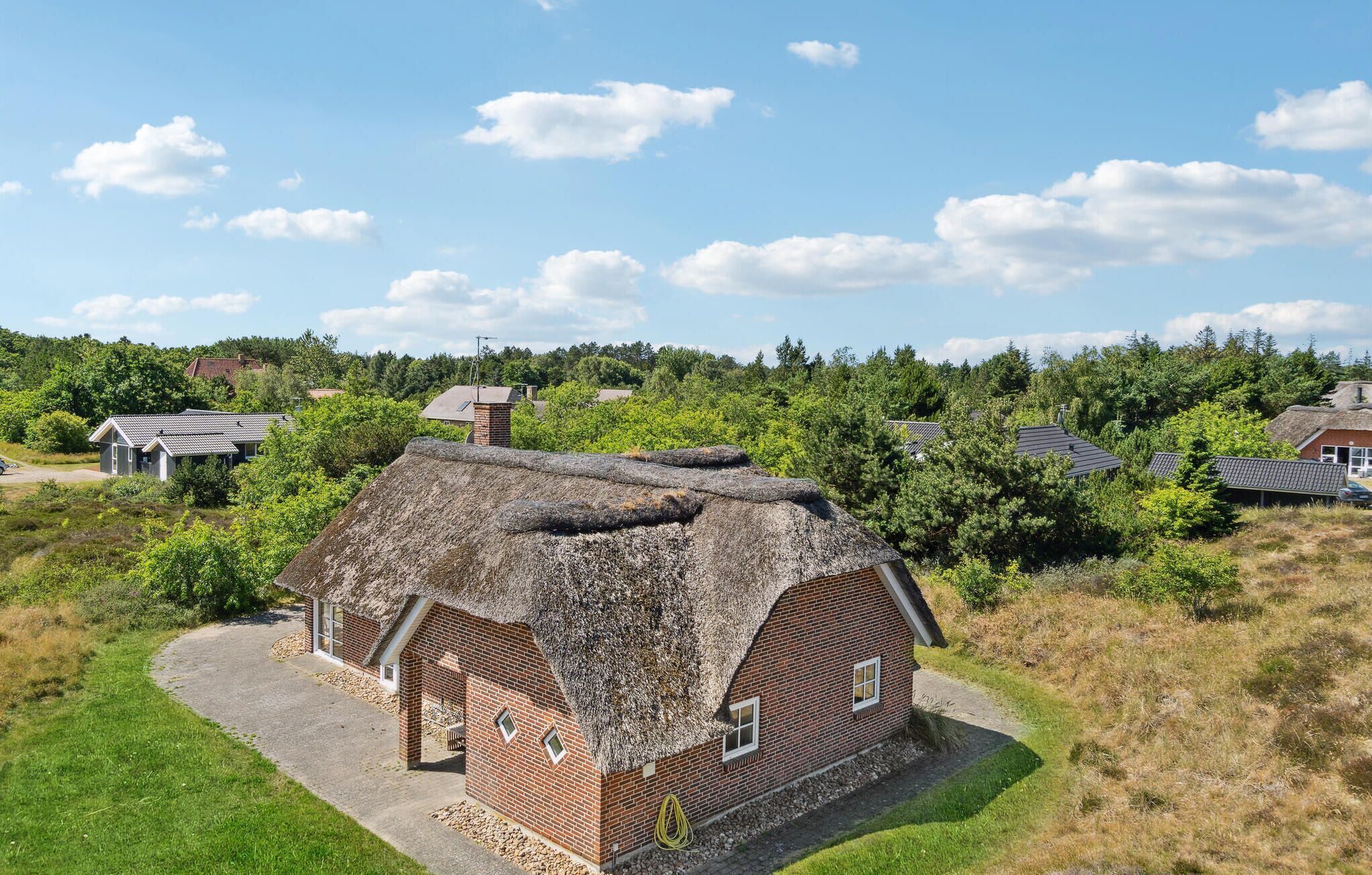 Een rieten huis met een bakstenen gevel, omringd door gras en bomen.