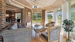 A spacious room with a high ceiling, brick walls, and large windows offering a view of greenery. - 4 bedroom gorgeous home in Rømø (Rømø)