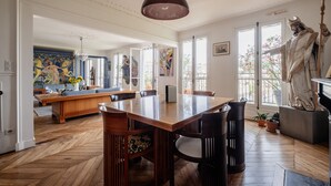 A spacious room with a large wooden dining table, a statue, and a view of a balcony. - Eclectic Eminence, by Veeve (Paris)